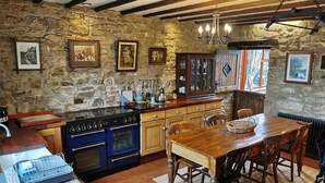 A rustic kitchen with stone walls, wooden cabinets, a large stove, and a dining table with chairs.