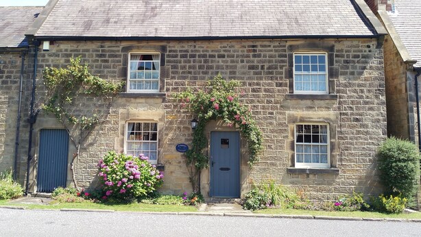 A stone cottage with a blue door, two windows, and a chimney.