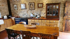 A rustic kitchen with a wooden table and chairs, a stone wall, and various kitchen appliances.