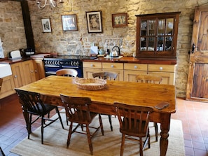 A rustic kitchen with a wooden table and chairs, a stone wall, and various kitchen appliances. - Pathways Holiday Cottage a Delightful 18th Century Stone Cottage in Derbyshire (Alfreton)
