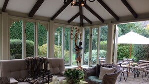 A conservatory with wicker furniture, a central table with candles, and a statue. - Gorgeous Village Barn, nr Banbury / Chipping Norton - Cotswolds, Oxfordshire (Shutford)
