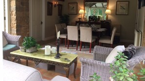 A dining area with a table set for four, surrounded by wicker chairs, a stone wall, and a mirror above the table. - Gorgeous Village Barn, nr Banbury / Chipping Norton - Cotswolds, Oxfordshire (Shutford)