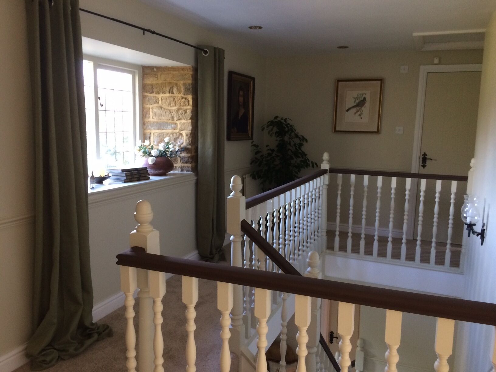 A staircase with white balusters and a dark handrail, leading to a landing with a window and a stone wall.