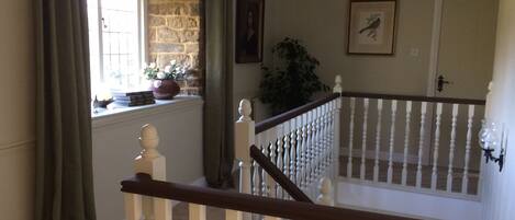 A staircase with white balusters and a dark handrail, leading to a landing with a window and a stone wall.