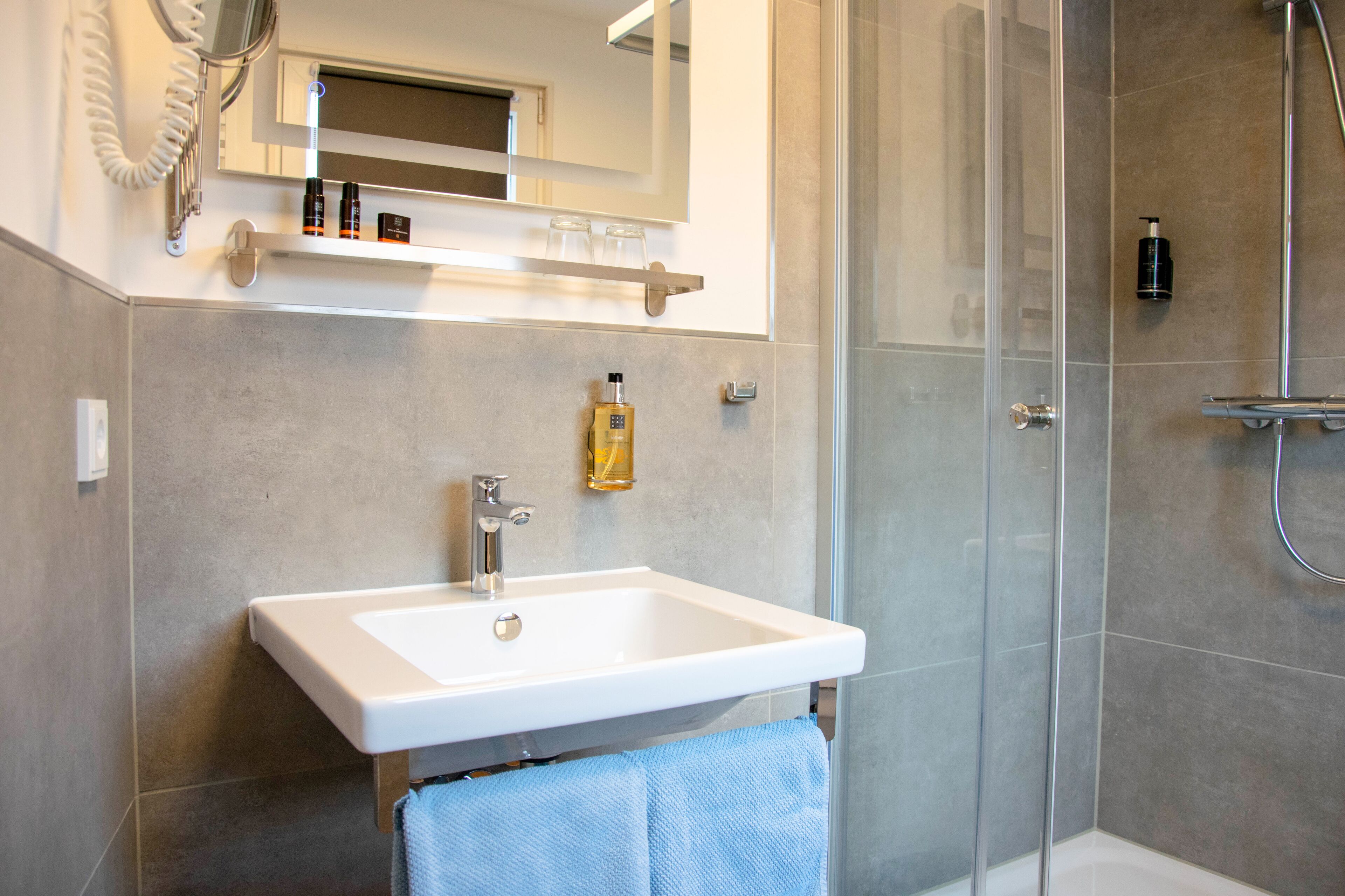Ein modernes Badezimmer mit einem weißen Waschbecken, einer Duschkabine aus Glas und einem Spiegel über dem Waschbecken.
