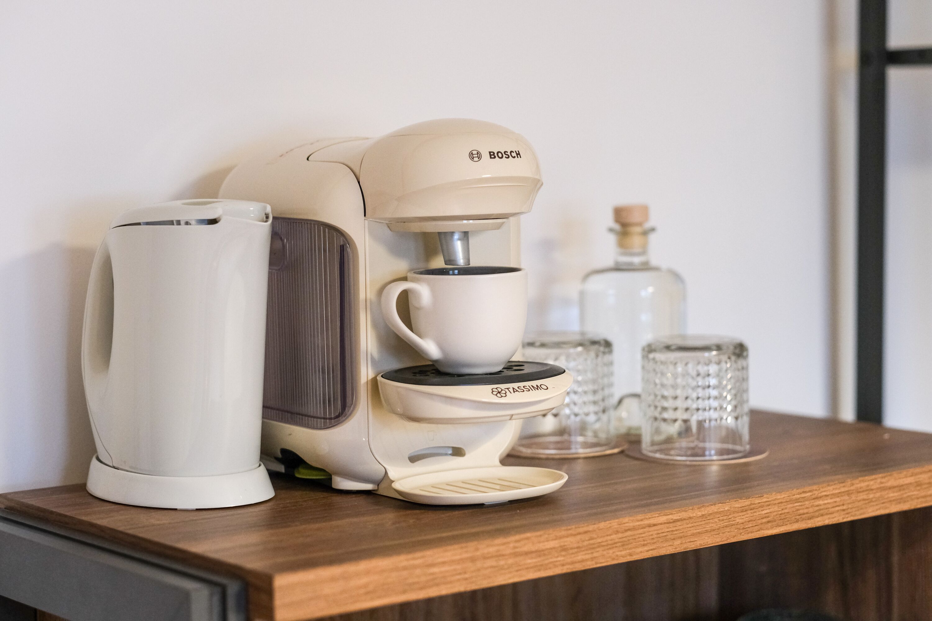 A coffee machine with a cup holder and a water dispenser on a wooden shelf.