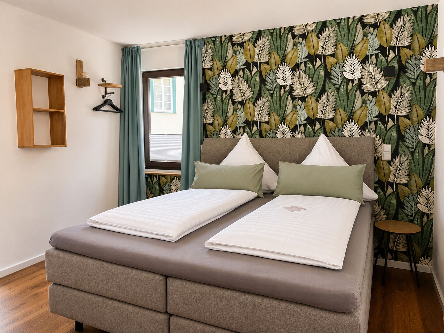 A double bed with a headboard, a wooden shelf, and a window with curtains.