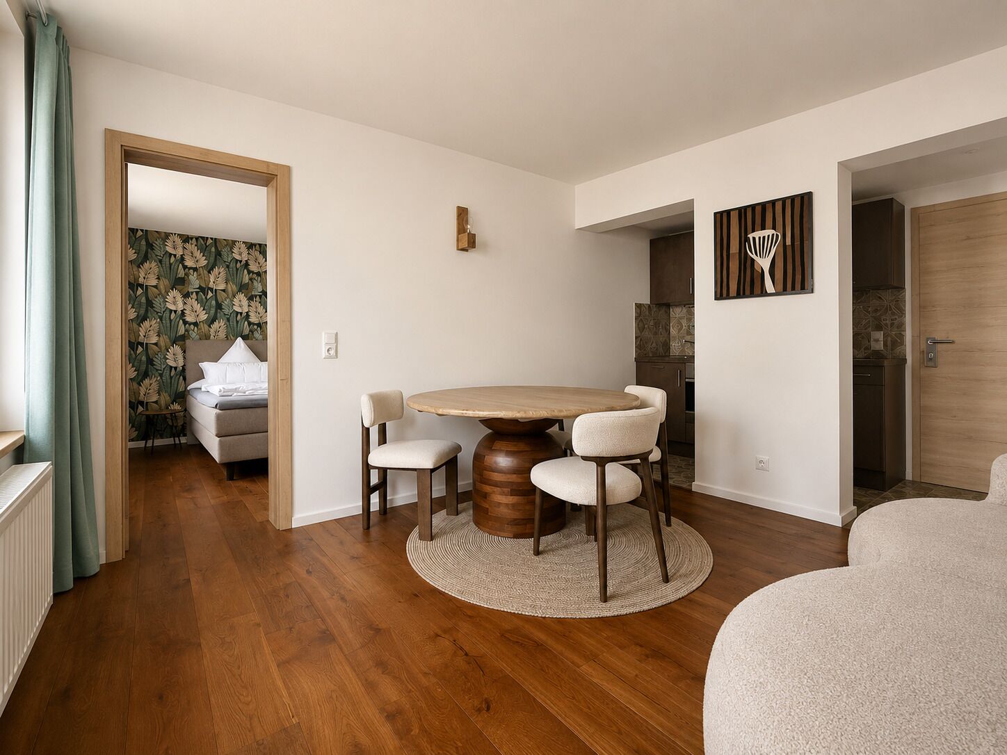 A modern living room with a round wooden table, two upholstered chairs, a sofa, and a kitchen in the background.