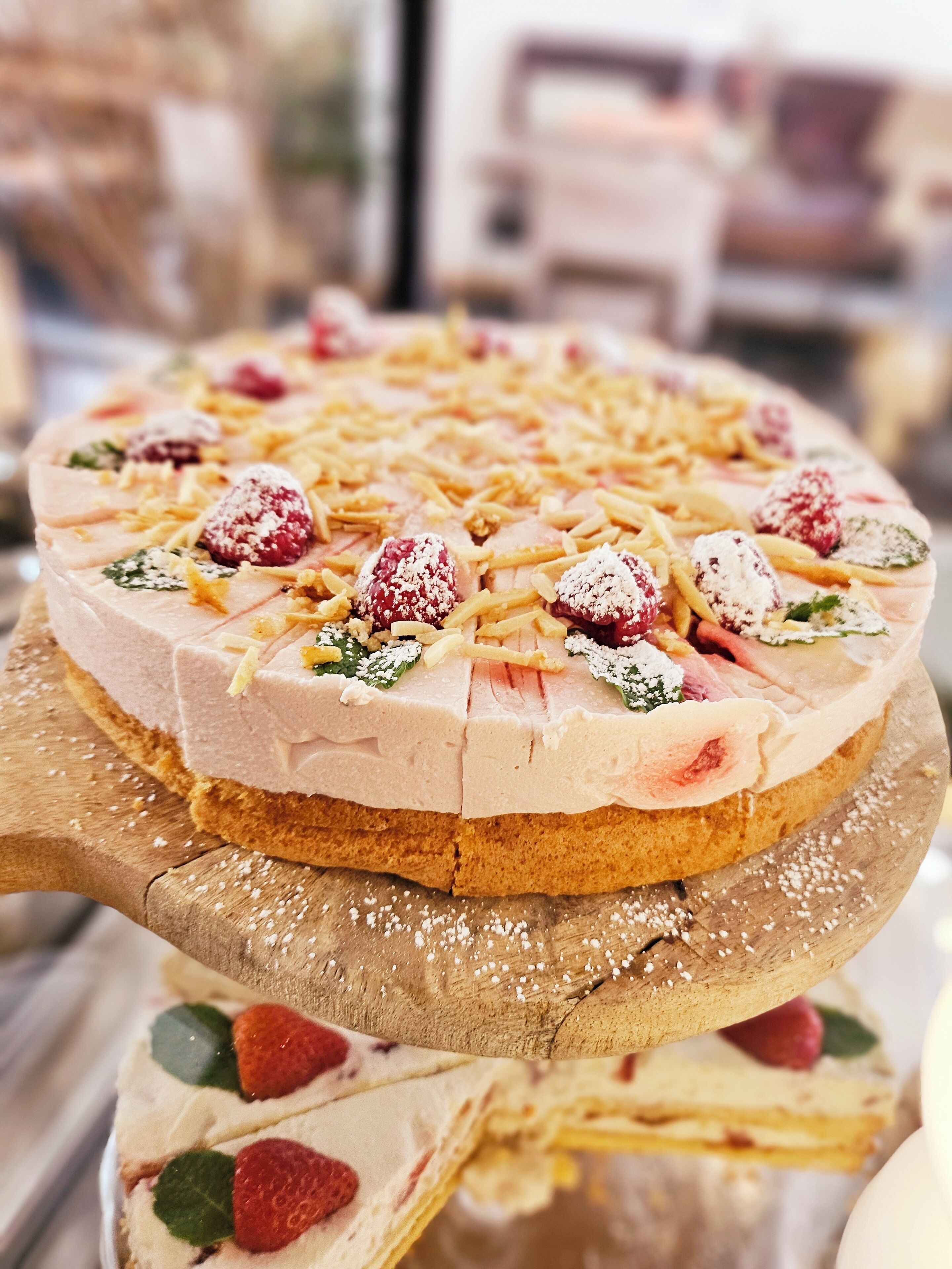 A multi-layered dessert with various toppings, including raspberries and shredded cheese, displayed on a wooden board.
