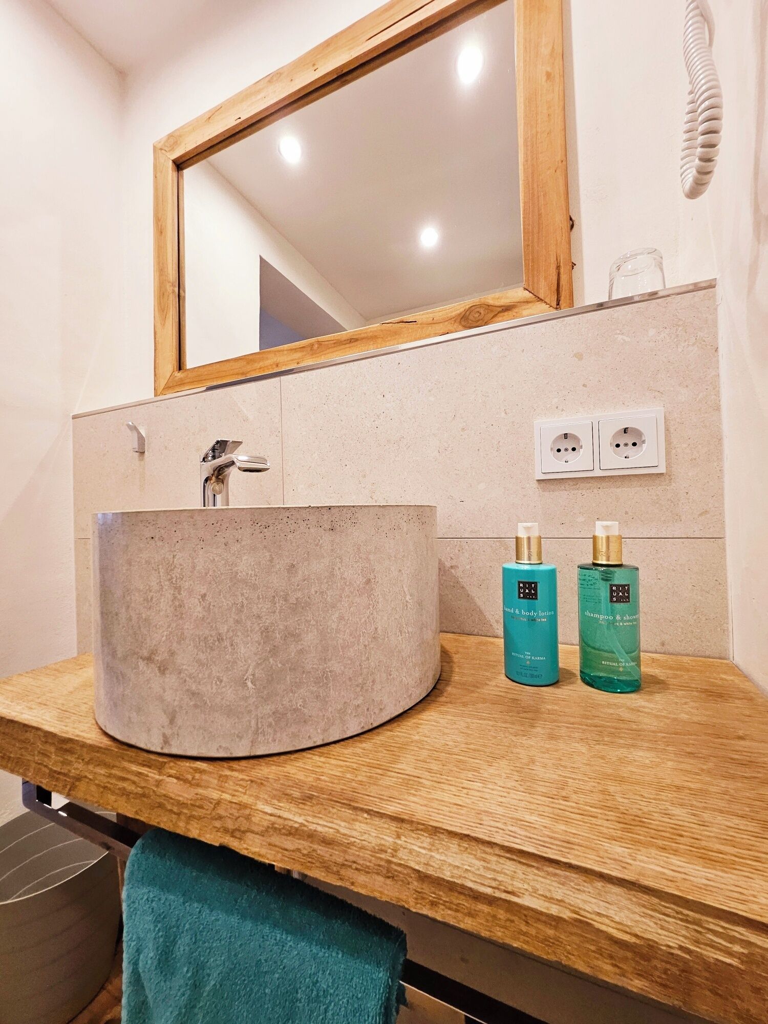 A bathroom with a round sink, wooden countertop, and a mirror above. There are two bottles of shampoo and body lotion on the counter.