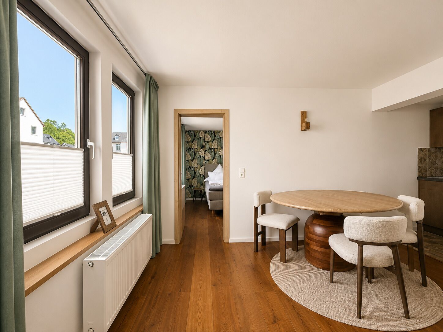 A modern room with a round wooden table, four chairs, a radiator, and a window with blinds.