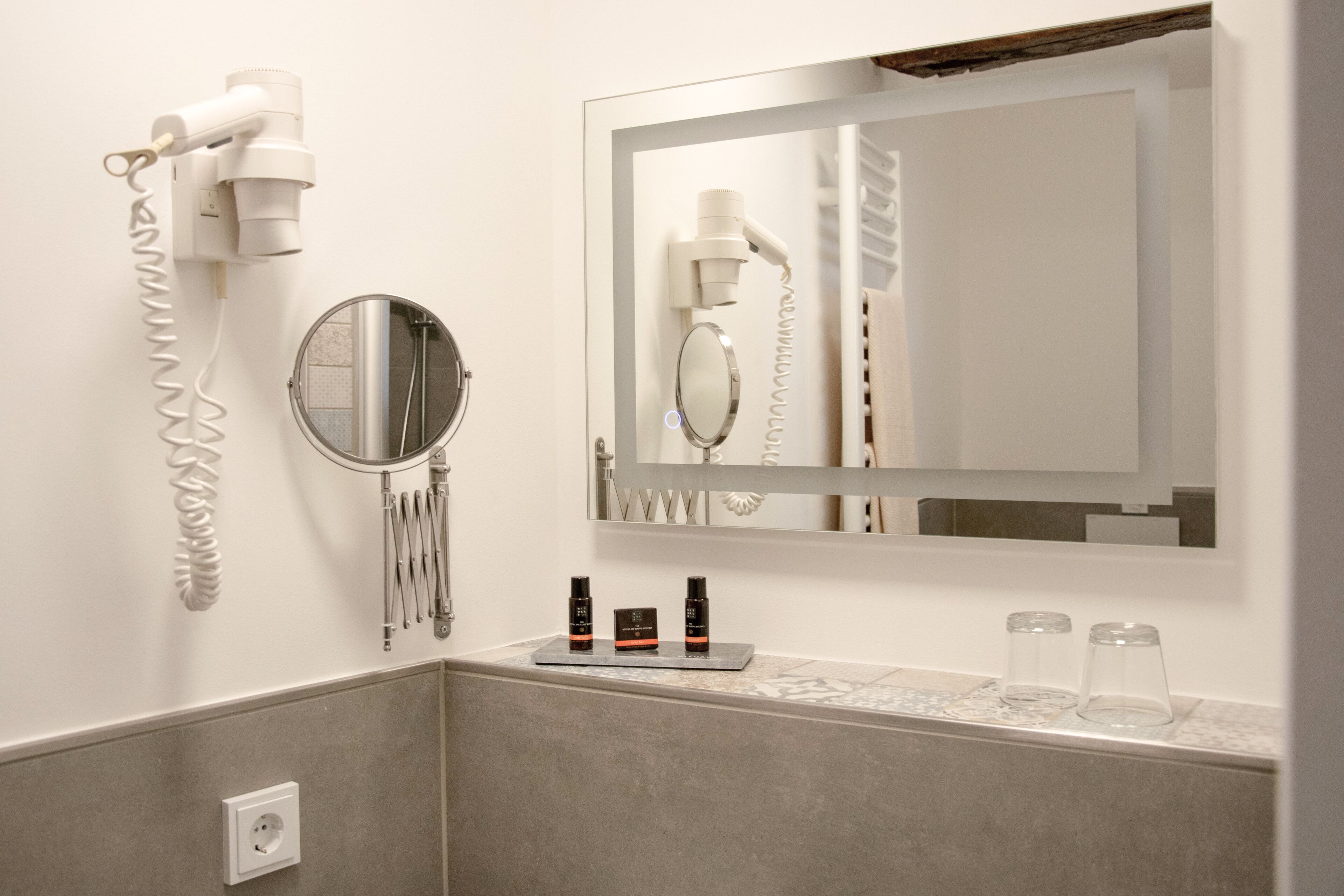 A bathroom with a hairdryer, mirror, and toiletries on the counter.
