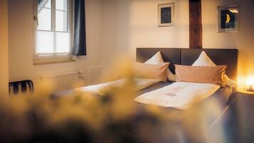 A hotel room with a bed, a radiator, a window with blinds, and two framed pictures on the wall.