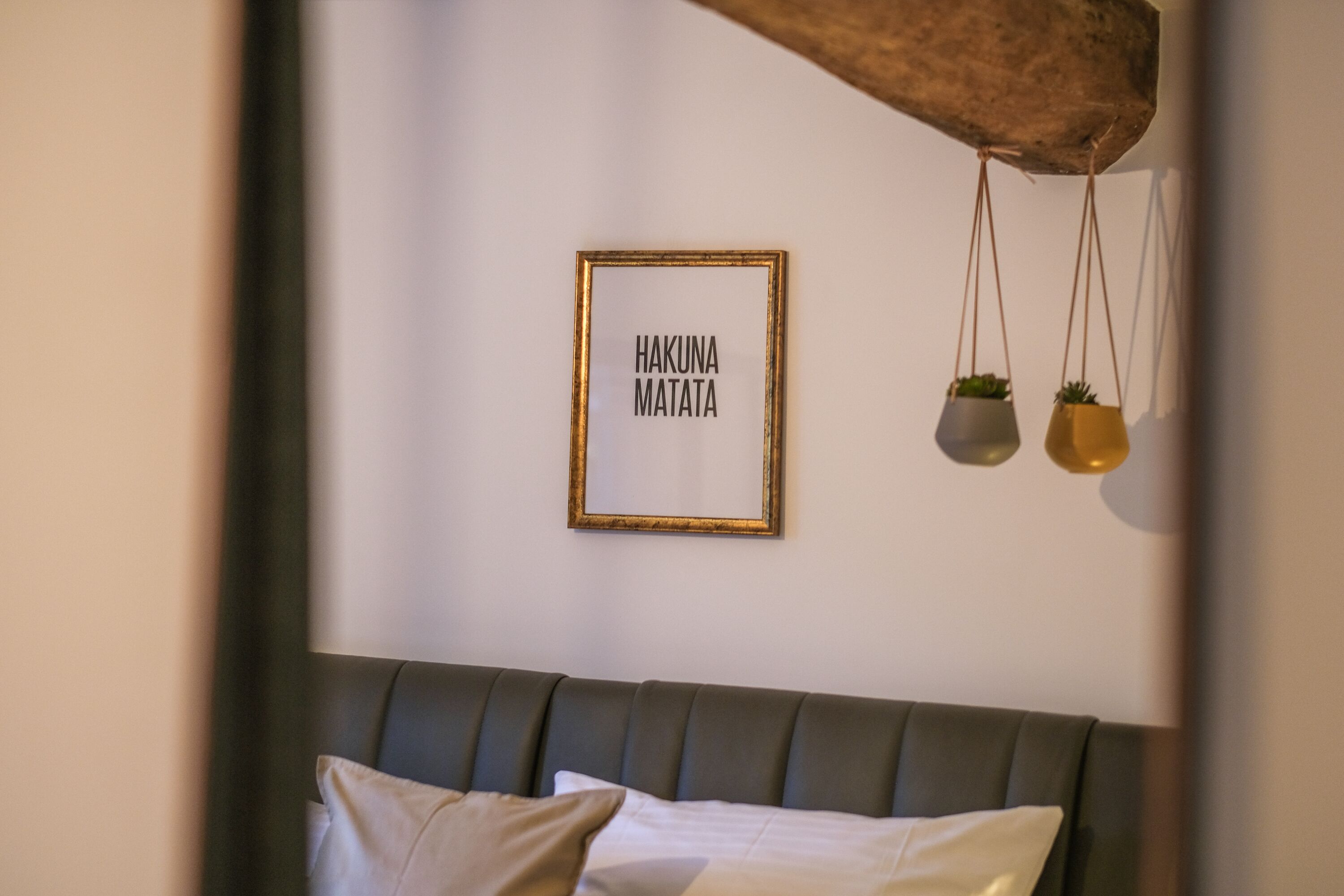 Ein gerahmtes Schild mit Text, ein Bett mit Kissen und zwei hängende Pflanzgefäße.