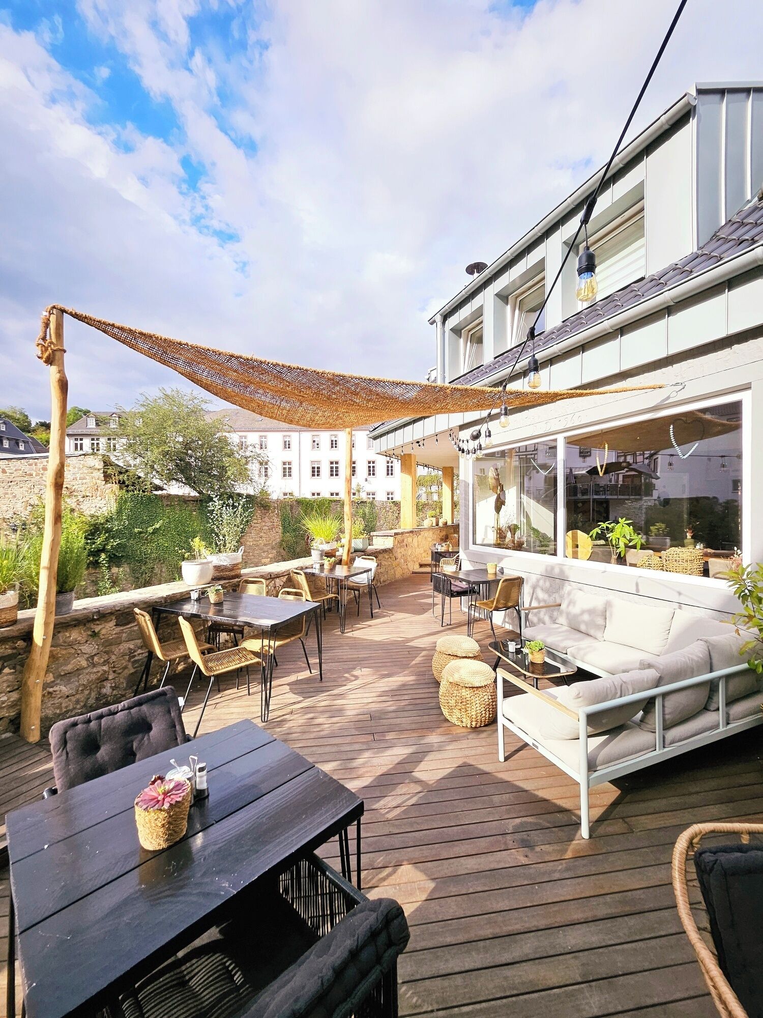 Een terras buiten met houten vloeren, rieten meubels en een witte bank.