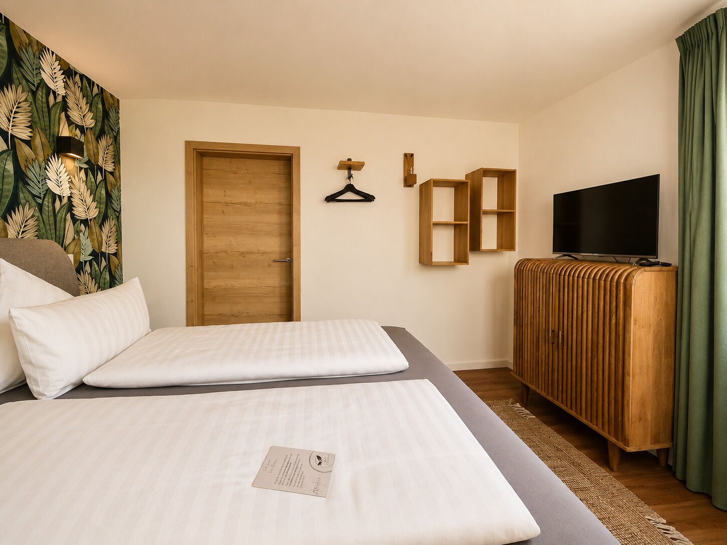 A hotel room with two beds, a wooden wardrobe, a television, and a wall-mounted shelf.