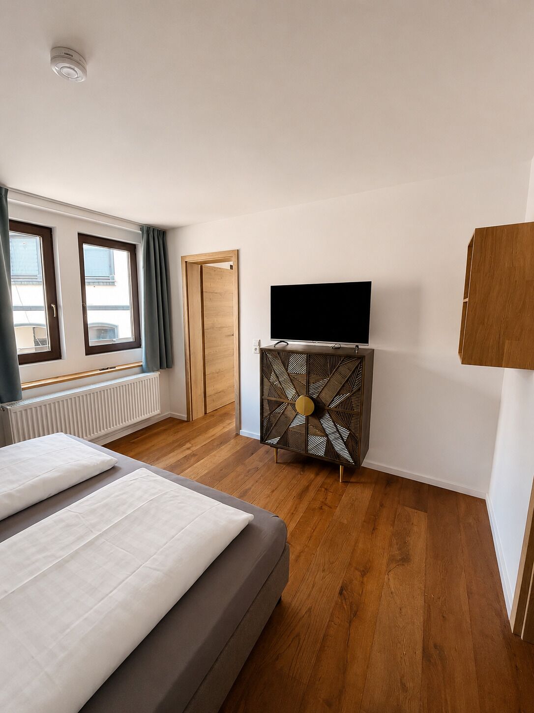 A bedroom with a bed, a TV on a cabinet, a wooden door, and a window.