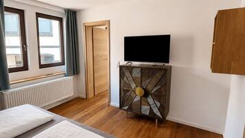 A bedroom with a bed, a TV on a cabinet, a wooden door, and a window.