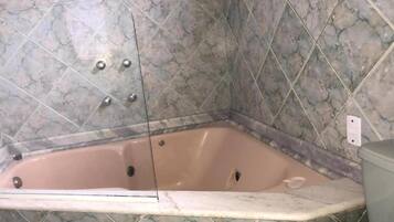 Una bañera en esquina con una pared de mármol y un banco de madera.