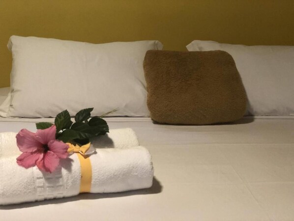 A neatly made bed with white and brown pillows, a rolled white towel with a pink flower, and a green plant. - Pousada Beira Mar (Garopaba)