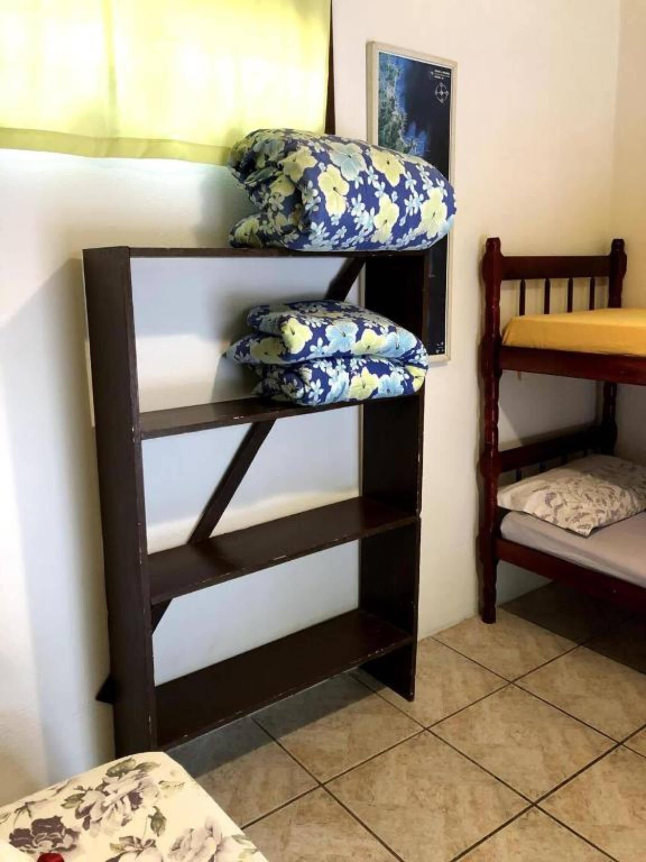 Un lit superposé avec une structure en bois et une étagère inférieure agrémentée de coussins à motifs floraux.