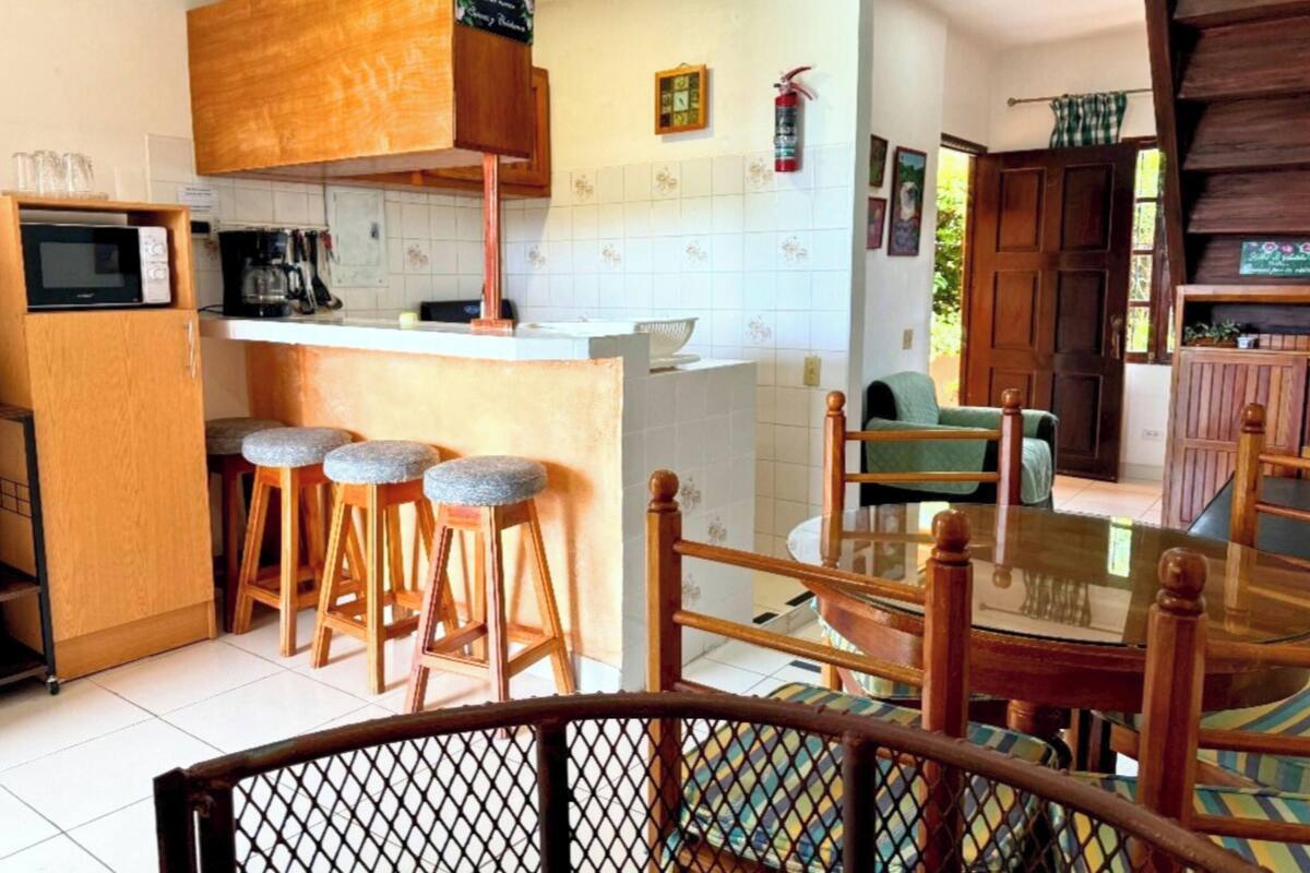 Cozinha compacta com micro-ondas, banquetas e mesa de jantar com cadeiras.