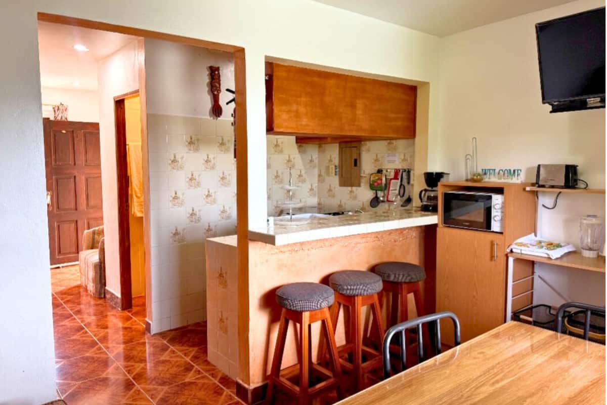 Uma cozinha compacta com bancada de madeira, banquetas, micro-ondas e uma pequena mesa de jantar.
