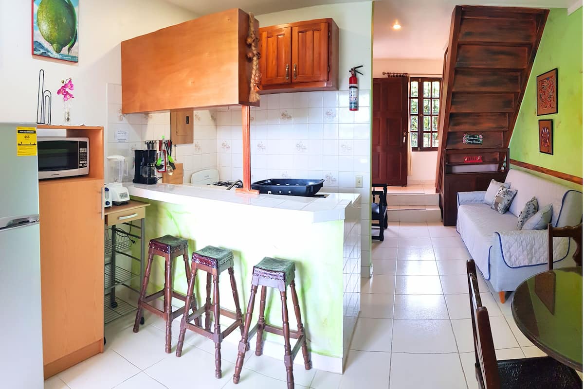 Cozinha compacta com ilha central, banquetas de madeira, micro-ondas e máquina de café.