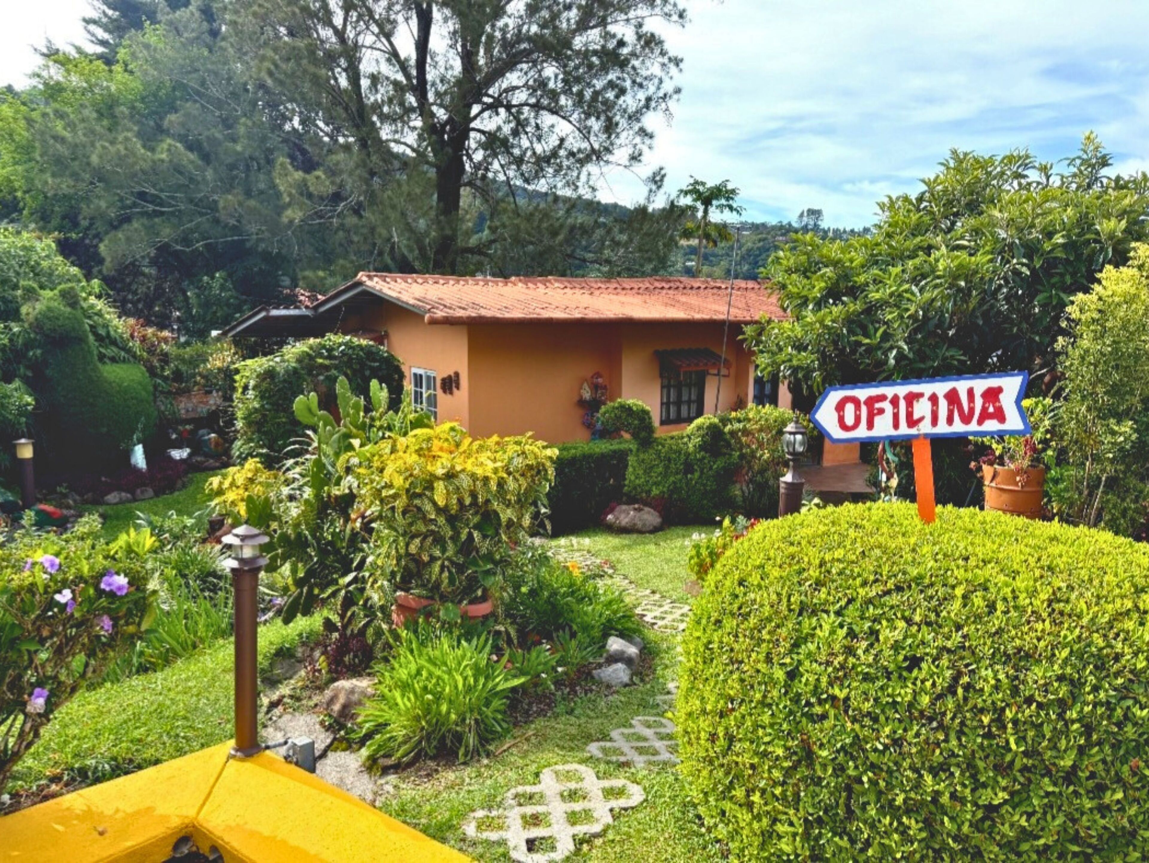 Una casa con un letrero que dice "Oficina", rodeada de vegetación exuberante y un sendero de jardín.