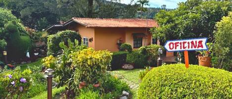 Una casa con un letrero que dice "Oficina", rodeada de vegetación exuberante y un sendero de jardín.