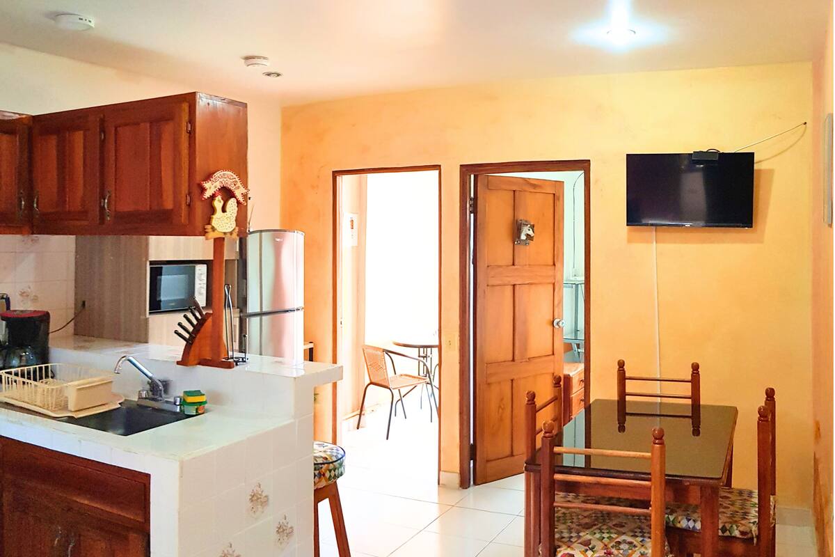 Uma cozinha com armários de madeira, geladeira, micro-ondas e uma área de jantar com mesa e cadeiras.