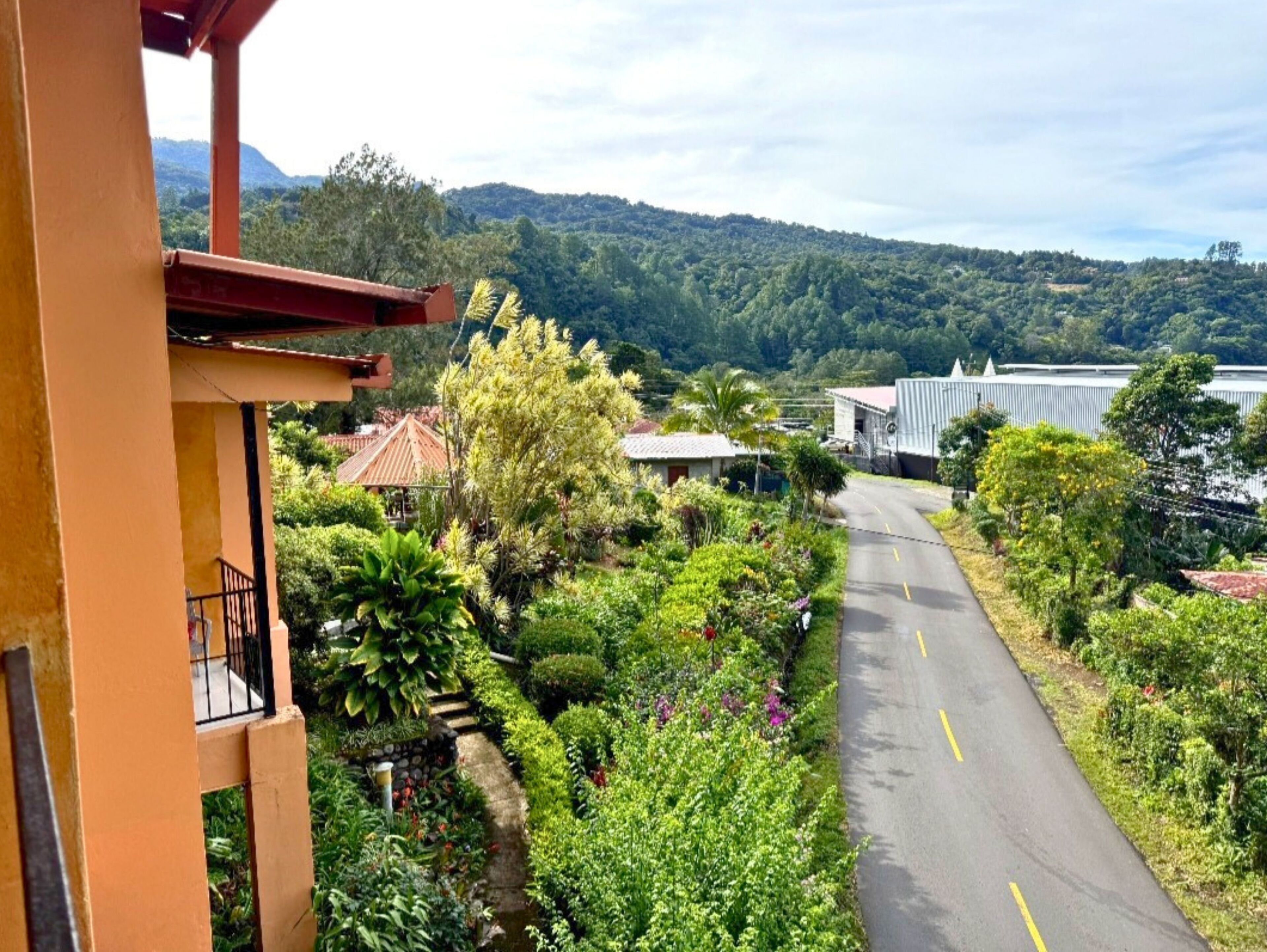 A road with lush greenery and a building with a balcony.