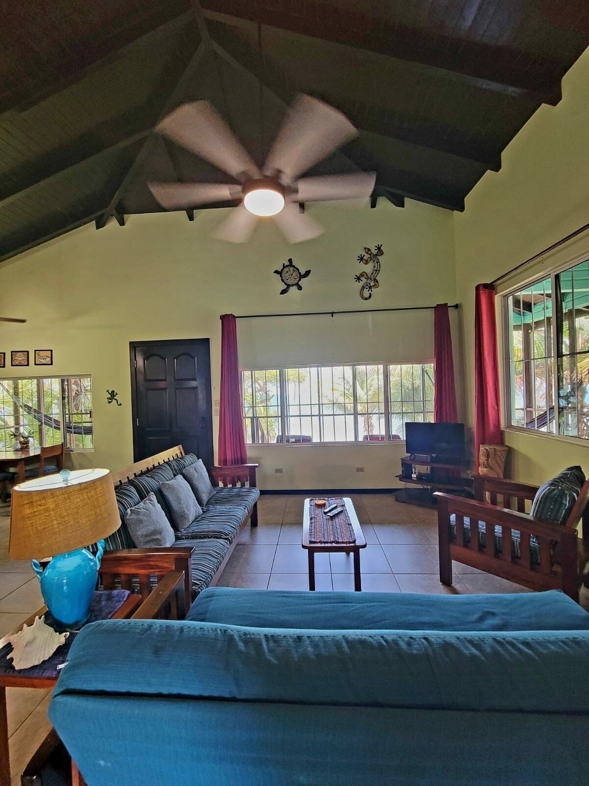 A spacious living room with a ceiling fan, a sofa, a television, and a large window with curtains.