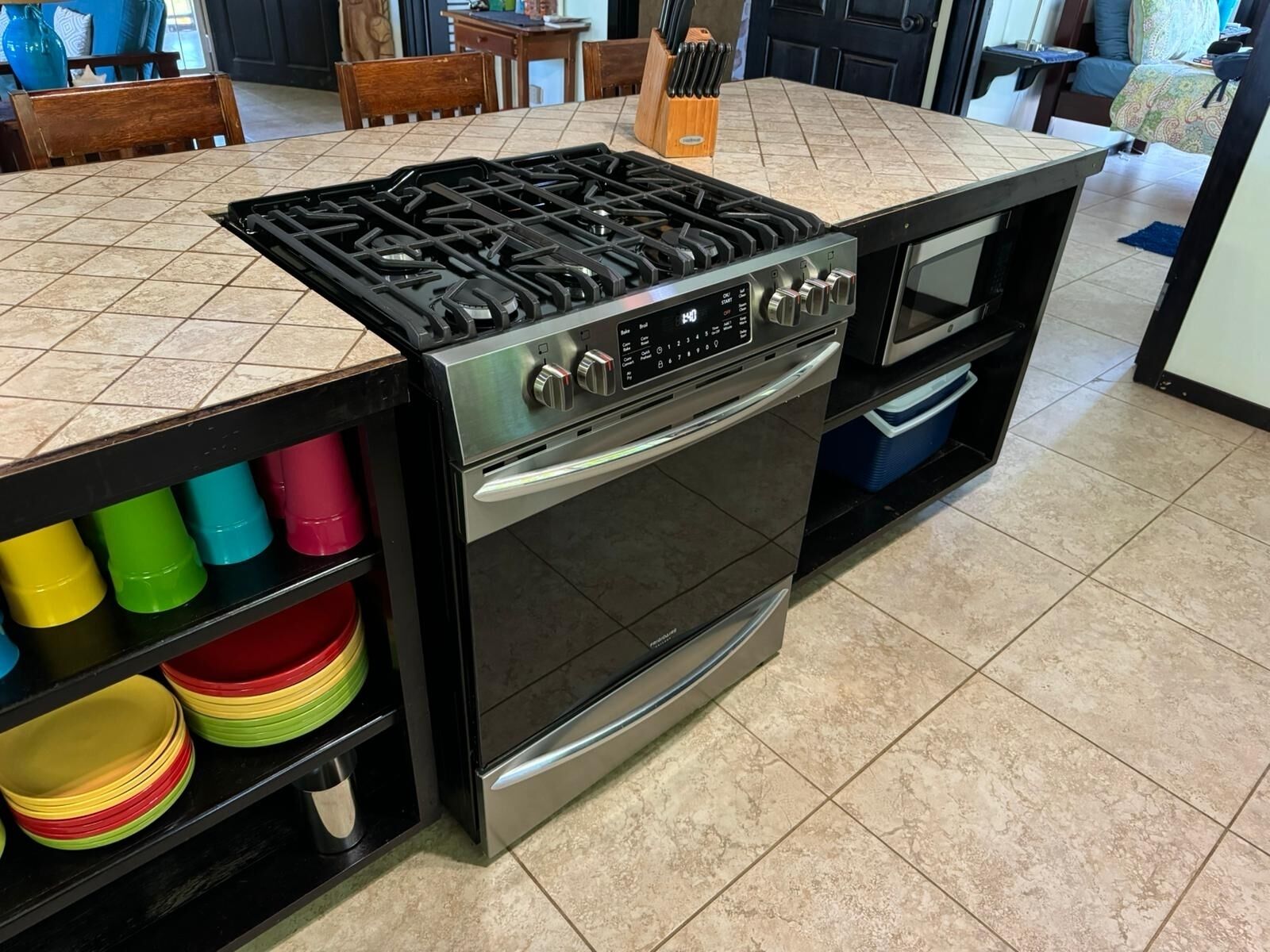 Une cuisine équipée d’une cuisinière à gaz, d’un four et d’une étagère où sont rangés des bols de différentes couleurs.