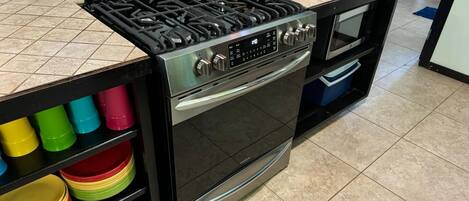 Une cuisine équipée d’une cuisinière à gaz, d’un four et d’une étagère où sont rangés des bols de différentes couleurs.