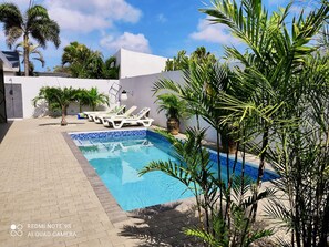 A swimming pool with lounge chairs, surrounded by plants and a white wall.