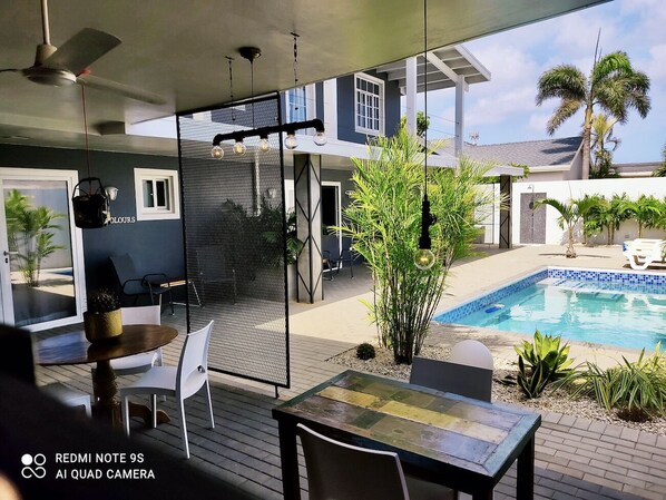 An outdoor patio area with a pool, seating, and a covered seating area.