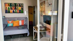 A room with a grey sofa, colorful cushions, a small table with a bowl, and a glass partition.