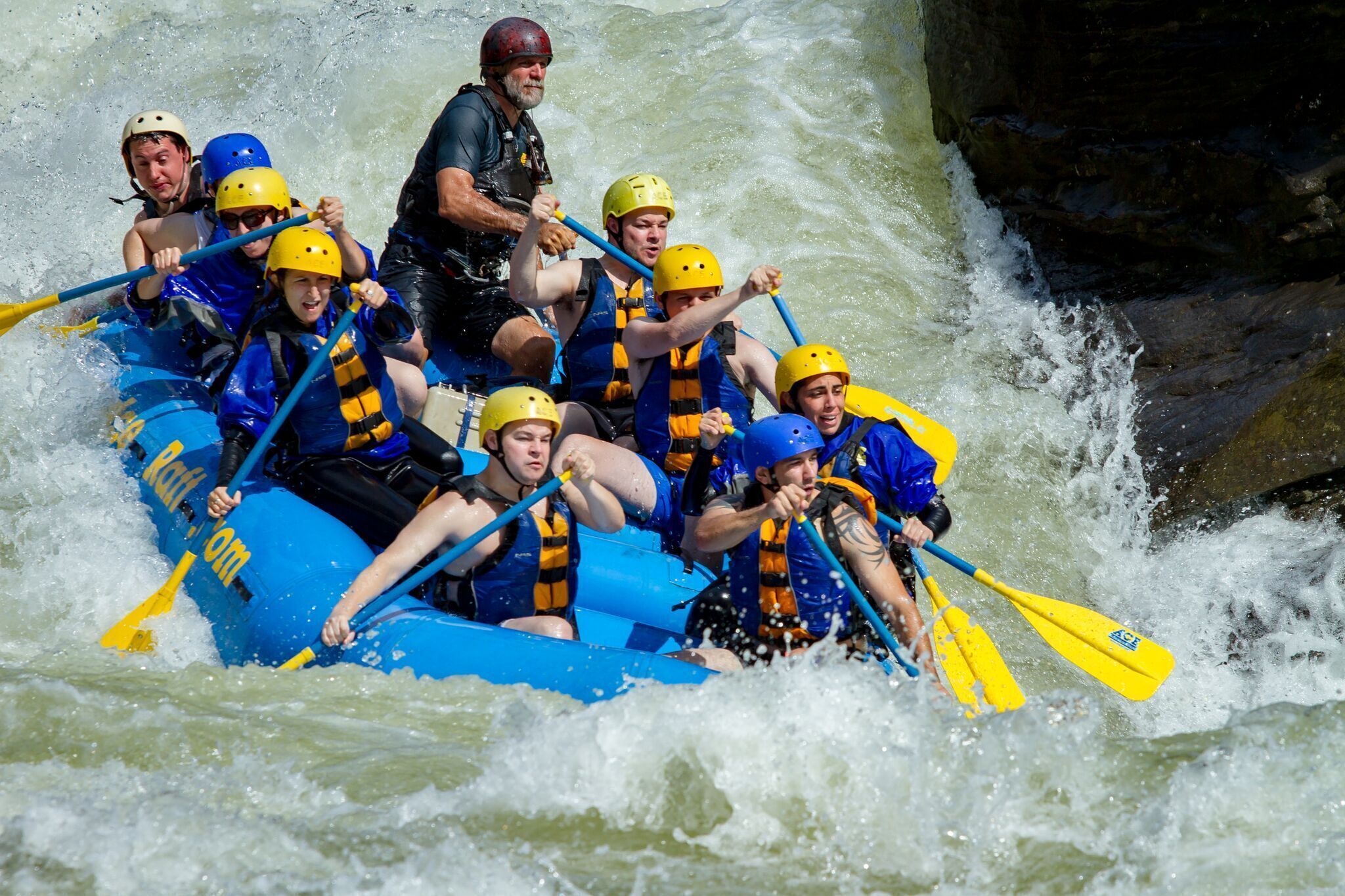 A group of people in a blue raft navigating through a river with rapids.
