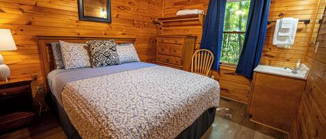Une pièce de cabane en bois comprenant un lit, une commode, une chaise et une fenêtre avec des rideaux.