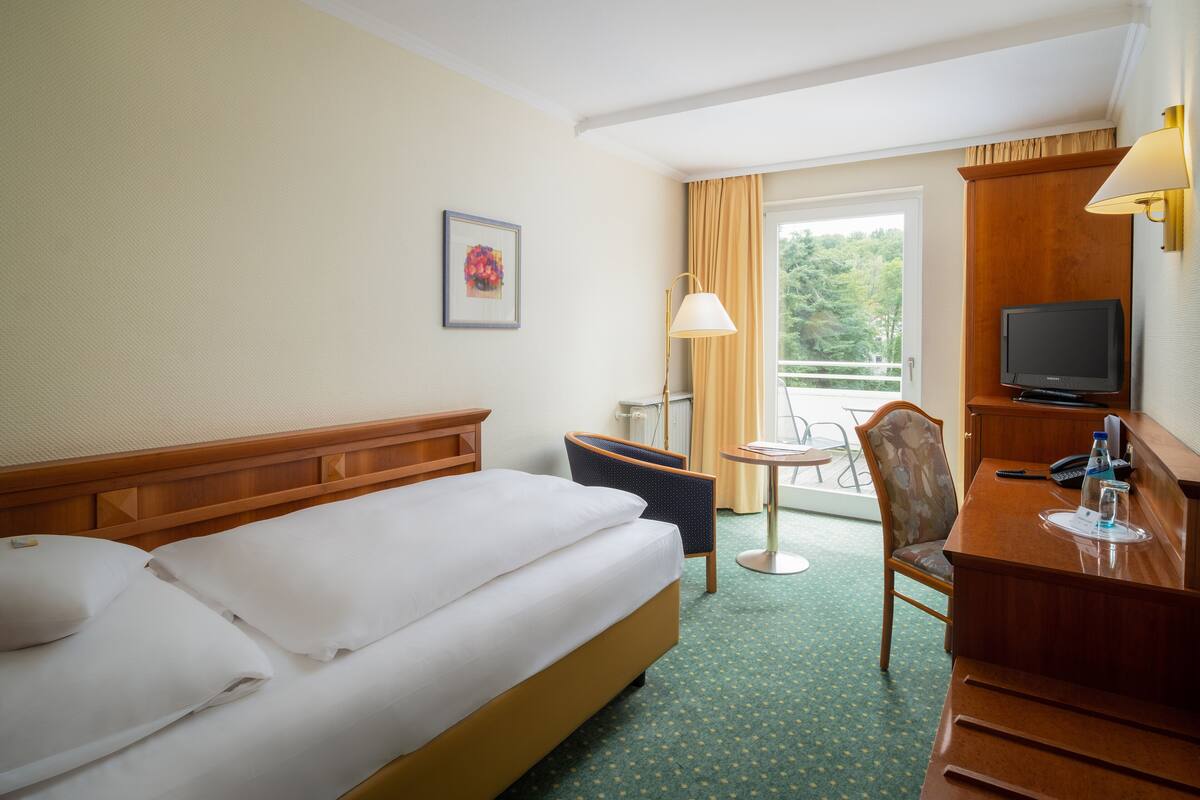 Habitación de hotel con cama, escritorio con televisor, silla y una mesita de noche con lámpara.
