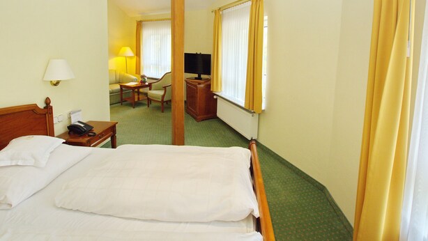 Habitación de hotel con cama, escritorio, silla, lámpara y televisor.