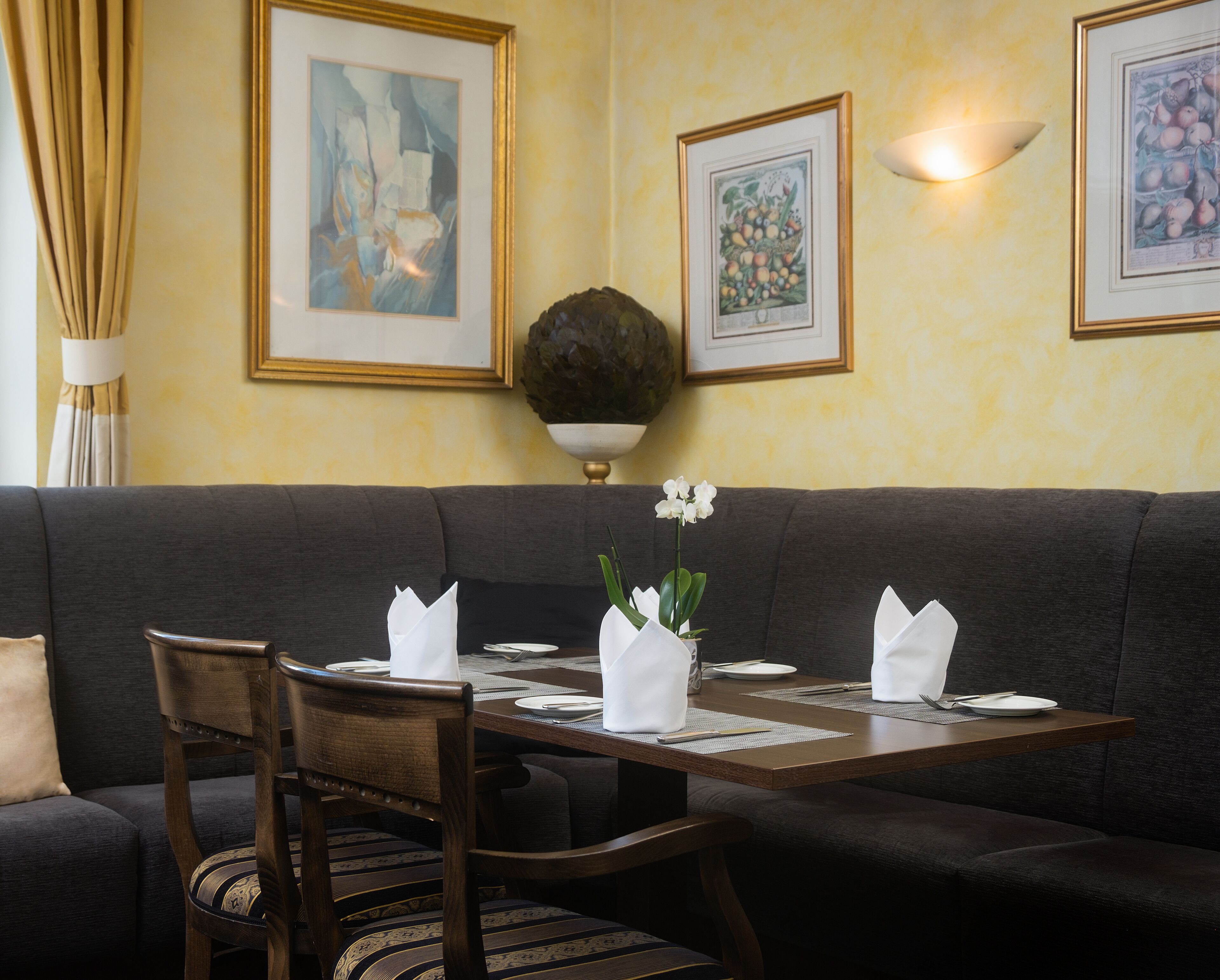 A dining area with a dark-colored sofa, wooden chairs, a dining table set with plates, cutlery, and a vase with white flowers.