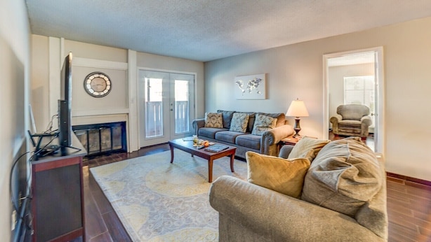 A living room with a sofa, coffee table, and lamp. There is a fireplace, a clock, and a door leading to a balcony. - Stay in a classically designed apt near ORU, exercise trails, and restaurants! (Tulsa)