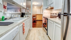 A narrow kitchen with white cabinets, a stainless steel refrigerator, and a wooden floor. - Stay in a classically designed apt near ORU, exercise trails, and restaurants! (Tulsa)