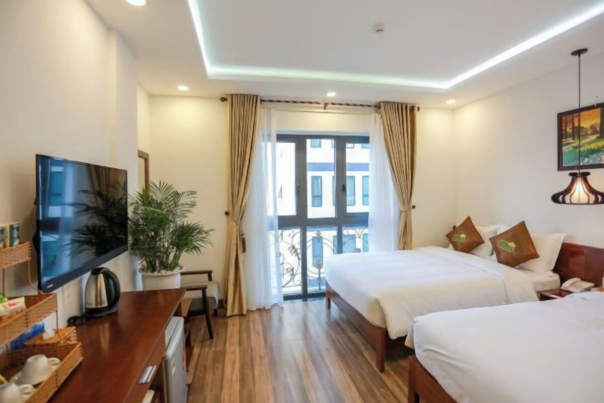 Habitación de hotel con dos camas, televisión, escritorio con computadora y ventana con cortinas.