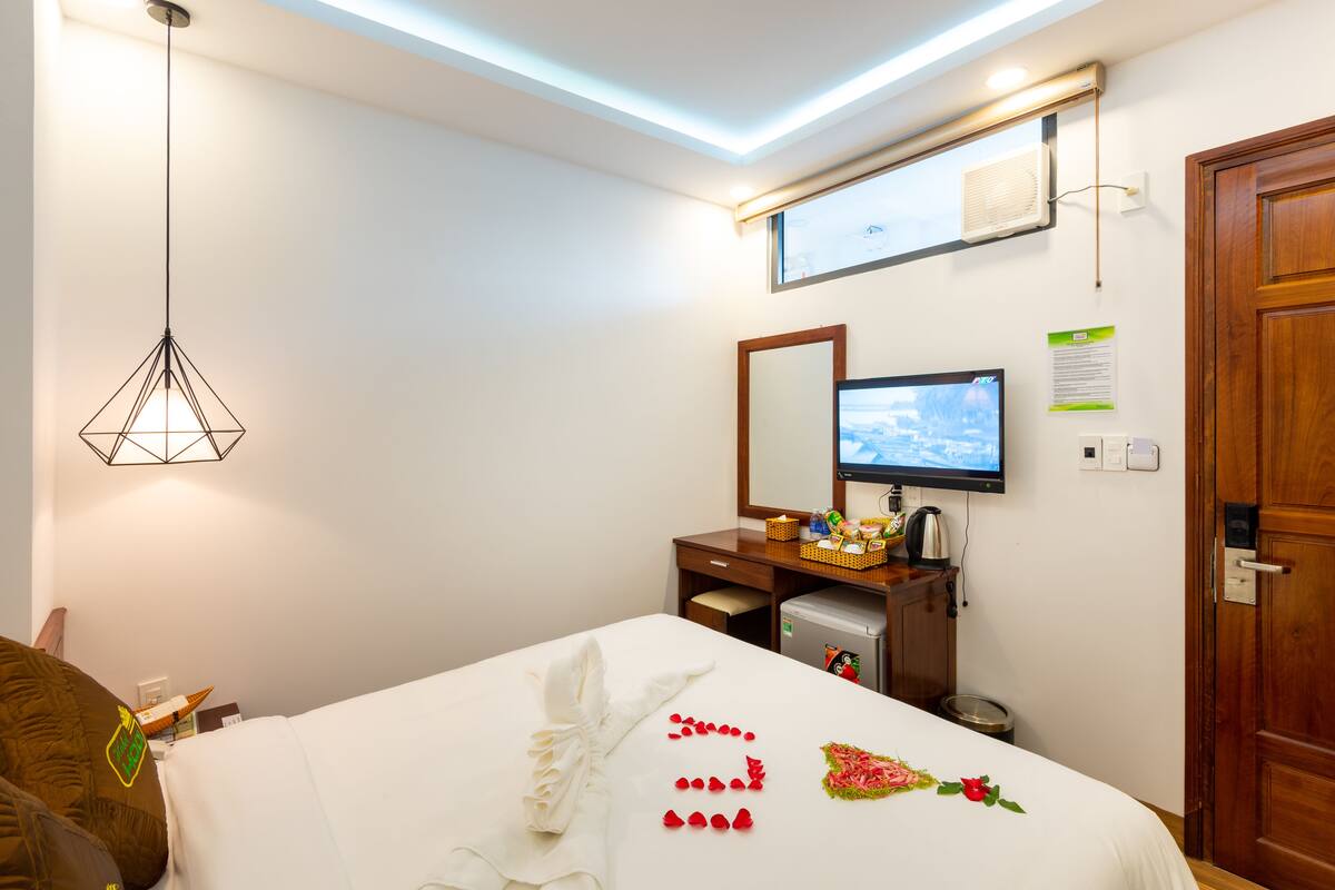 Una habitación de hotel con cama, escritorio con computadora, televisor y lámpara en el techo.