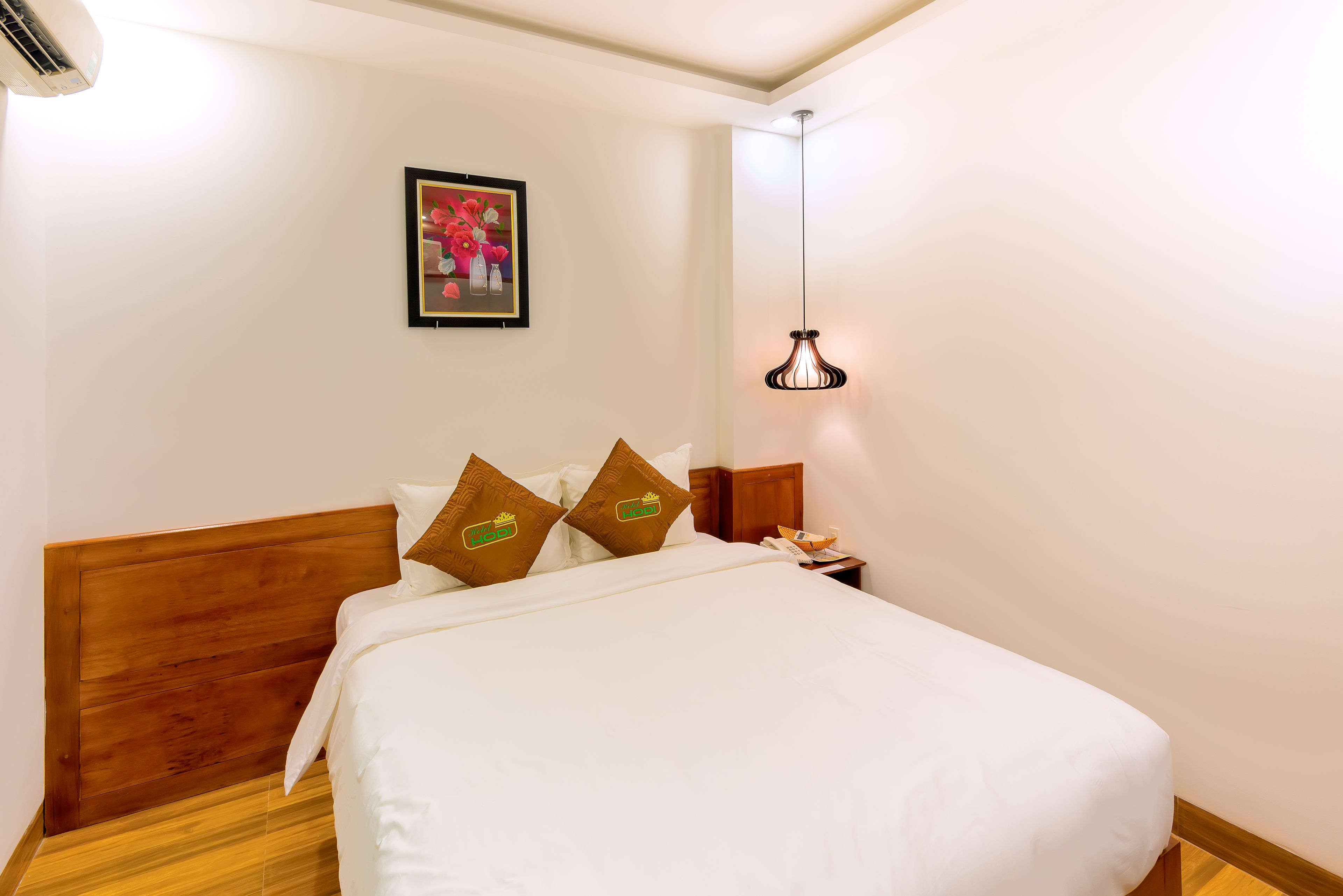 A neatly made bed with white bedding and two decorative pillows, a bedside table with a lamp, and a framed picture on the wall.