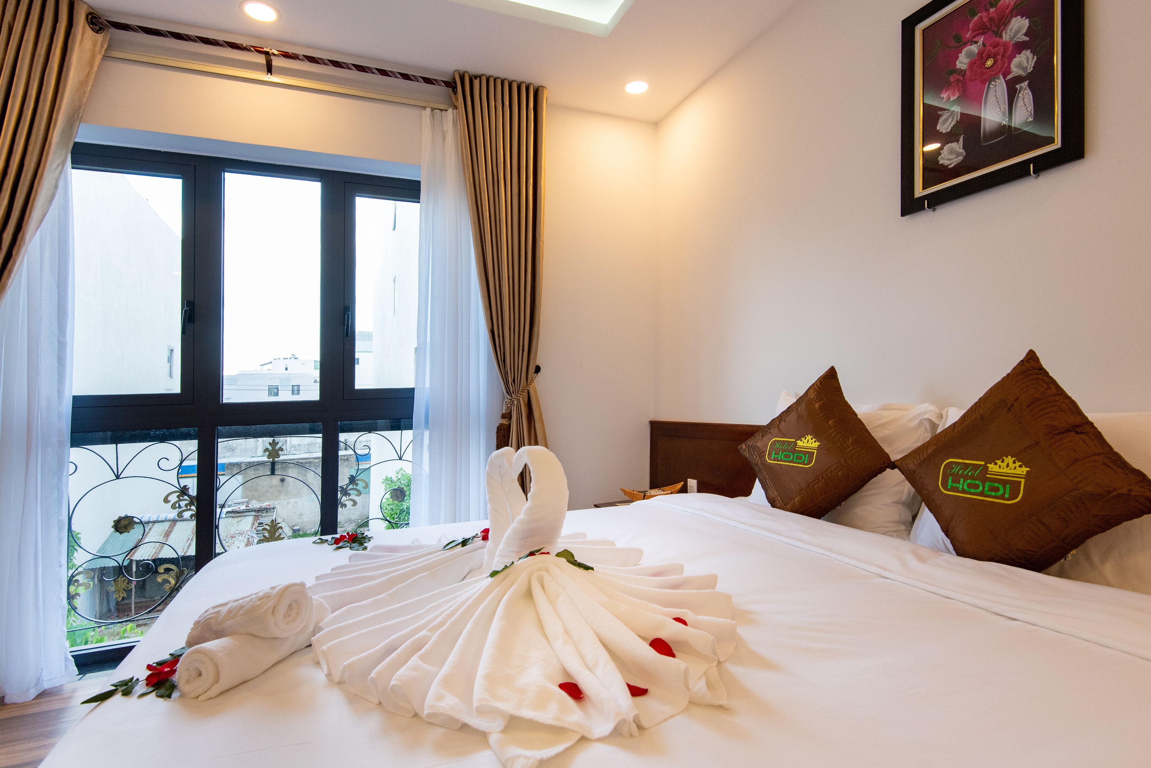 Habitación de hotel con una cama decorada con una grúa de toalla, un balcón con vistas y dos almohadas con el logotipo del hotel.