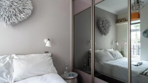 Een hotelkamer met een bed, nachtkastje met lamp, spiegel en decoratieve wanddecoratie.
